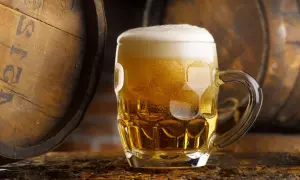 Boccale di birra dorata con schiuma, accanto a botti di legno. Un litro di birra calorie da gustare con moderazione.