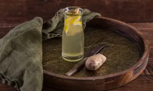 Szklana butelka z orzeźwiającą nalewką z imbiru i cytryny, obok świeży korzeń imbiru i nóż.