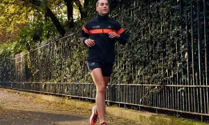 Kobieta w sportowym stroju biegnie po chodniku. Idealny przykład, jak się ubrać do biegania jesienią: lekka kurtka, spodenki i buty.