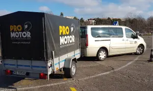 Przyczepa szkoły jazdy b+e "Pro Motor" z motocyklem w środku, obok biały bus.