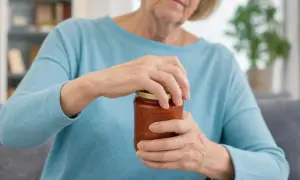 Donna anziana con debolezza arti superiori lotta per aprire un barattolo di salsa.