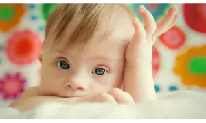 Bambino con sindrome di Down, occhi azzurri, mano sul viso. La vita delle persone Down è piena di amore e gioia.