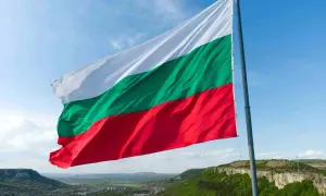 Flaga Bułgarii powiewa na tle błękitnego nieba nad malowniczym krajobrazem. Winieta Bułgaria.