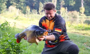 Wędkarz z dumą prezentuje okazałego karpia, który z pewnością nie jest ani sieją, ani sielawą.