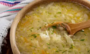Kapuśniak w drewnianej misce z drewnianą łyżką, ozdobiony szczypiorkiem.