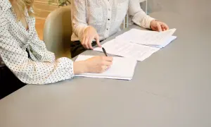 Dwie kobiety omawiają prosta umowa na wykonanie usługi. Jedna pisze w notatniku, druga przegląda dokumenty.