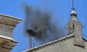 Gęsty, czarny dym wydobywa się z komina na tle błękitnego nieba. Nie jest to biały dym, lecz oznaka intensywnego spalania.