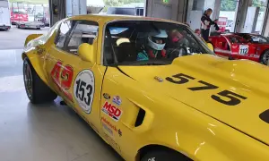 Gul Firebird 69 med nummer 153 och 575 redo för race. En förare i hjälm sitter bakom ratten.