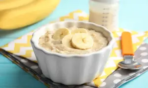 Ein Schüsselchen mit Bananen-Abendbrei, perfekt zum abendbrei selber machen. Daneben eine Babyflasche und ein Löffel.