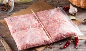 Zamrożone mięso mielone w woreczku, gotowe do rozmrożenia. Obok czosnek, pieprz i chili.