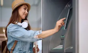 Kobieta w słomkowym kapeluszu korzysta z bankomatu, by wypłacić pieniądze. W Hiszpanii obowiązuje euro.