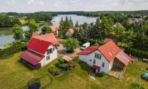 Malownicze agroturystyka nad jeziorem. Domy z czerwonymi dachami, zielony trawnik, trampolina i piękny widok na wodę.