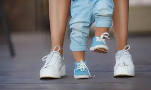 Dziecko w niebieskich bucikach i dorosły w białych sneakersach na drewnianym tarasie.