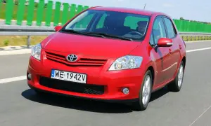 Czerwony Toyota Auris 2010 jedzie autostradą. Kierowca w czapce prowadzi auto.