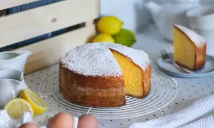 Una torta paradiso sofficissima, cosparsa di zucchero a velo, con spicchi di limone e uova fresche.