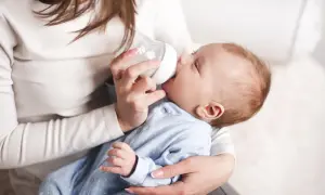 Matka karmi dziecko butelką. Uważaj na przekarmienie niemowlaka mlekiem modyfikowanym objawy, by uniknąć problemów.