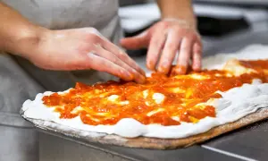 Händer sprider tomatsås på pizzadeg. En del av en matlagningskurs i att baka pizza.