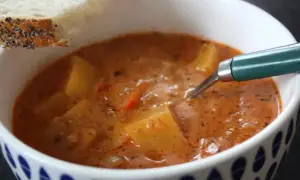 En skål med mustig cowboy soppa med potatis och en bit bröd.