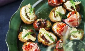 En grön tallrik med olika crostini topping: salami, tomat, ost och ruccola.