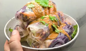 Kolorowe spring rolls z warzywami, polane kremowym sosem orzechowym i posypane orzeszkami. Idealne na lekki posiłek.