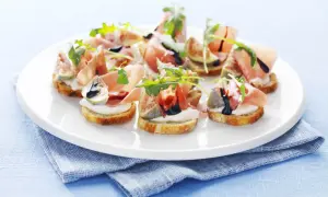 Köstliche italienische Crostini mit Prosciutto, Feigen, Mozzarella und Rucola auf einem weißen Teller.