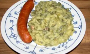 Omas Stielmus Rezept: herzhafte Grünkohl-Kartoffel-Masse mit einer deftigen Bratwurst auf einem Teller mit blauem Muster.