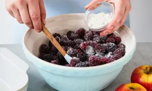 Hände mischen Brombeeren mit Zucker für schnelle und einfache Brombeeren Rezepte. Äpfel liegen daneben.