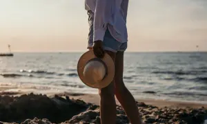 Sonnenuntergang am Kolberg Strand. Eine Frau hält einen Strohhut, während sie am Wasser entlang spaziert.