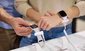Un homme montre comment charger une montre connectée à une femme. La montre est fixée à un support de démonstration.