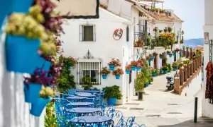 Callejuela encantadora en uno de los pueblos costeros de Málaga, con fachadas blancas, macetas azules y mesas de terraza.