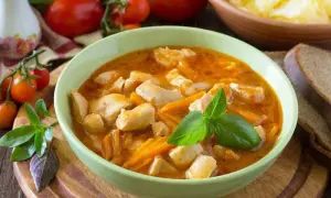 Aksamitny gulasz z piersi kurczaka z marchewką, udekorowany bazylią. Obok kromki chleba i miska purée ziemniaczanego.