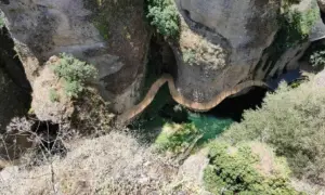 Un puente serpentea sobre el agua verde en el tajo de Ronda, rodeado de rocas y vegetación.