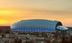 Stadion miejski w Poznaniu o zachodzie słońca, z niebieskimi światłami i charakterystycznym, falującym dachem.