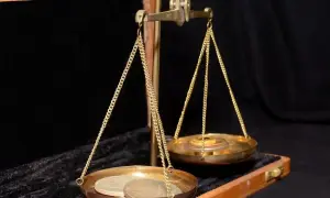 Złota waga szalkowa z monetami na jednej szalce i odważnikami na drugiej. Waga symbolizuje wartość, być może uncja złota.