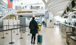 Kobieta z walizką i plecakiem idzie przez lotnisko w kierunku stanowisk odprawy.