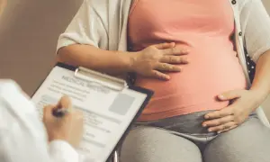 Lekarz notuje dane pacjentki, która trzyma dłoń na brzuchu. Obliczenia terminu porodu opierają się na regule Naegelego.