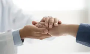 Lekarz w białym fartuchu trzyma za rękę pacjenta.
