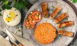 Saftige cevapcici im backofen, serviert mit Reis, Tomaten und einer cremigen Sauce.