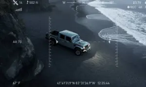 Un camion du futur gris, vu du ciel, roule sur une plage de sable noir. Les vagues de l'océan s'écrasent sur le rivage.