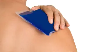 Main d'une personne appliquant une poche de glace bleue sur son épaule pour soigner une tendinite.