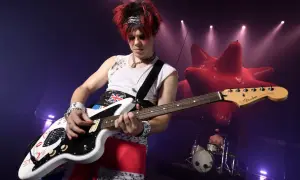 Yungblud gra na gitarze podczas koncertu w Warszawie. W tle czerwona, dmuchana instalacja i perkusista.