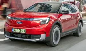 Czerwony Ford Explorer, nowoczesny SUV, pędzi po drodze, odbijając miejski krajobraz w swojej lśniącej karoserii.