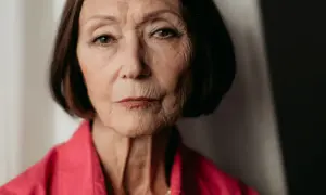 Portret starszej kobiety, Ewy Woydyłło, z widocznymi zmarszczkami, w różowej bluzce i perłach. Jej życie prywatne jest pełne doświadczeń.
