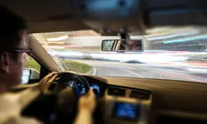 Conductor con gafas al volante de noche, con lluvia y luces de coches borrosas. El ASR de un coche ayuda a mantener la tracción en estas condiciones.