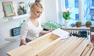 Kobieta składa drewniany stół, obok narzędzia i deski.