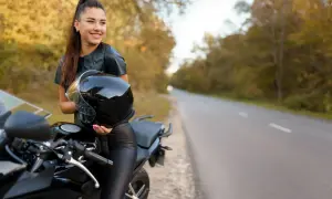 Uśmiechnięta kobieta na motorze, trzymająca kask, gotowa na podróż.