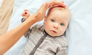 En hand smeker försiktigt huvudet på en bebis med blå ögon. Man kan ana den mjuka fontanell bebis.