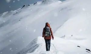 Persona con zaino cammina su un crinale innevato, mentre fiocchi di neve cadono dolcemente.