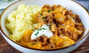 Herzhaftes Gericht mit Kartoffelpüree und geschmortem Kohl mit Hackfleisch als Beilage, garniert mit einem Klecks Sauerrahm und Petersilie.