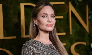 Angelina Jolie, jedna z najbardziej znanych aktorek Hollywood, w błyszczącej kreacji na tle złotych liter.